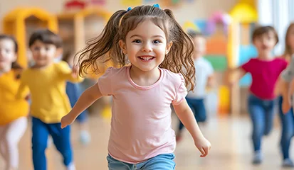 A young girl joyfully runs in a classroom filled with other children engaged in various activities