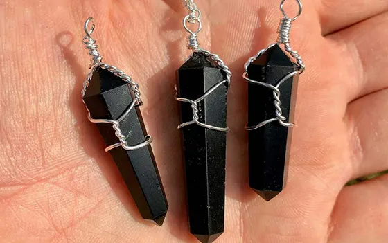 Three black onyx point pendants held in a hand